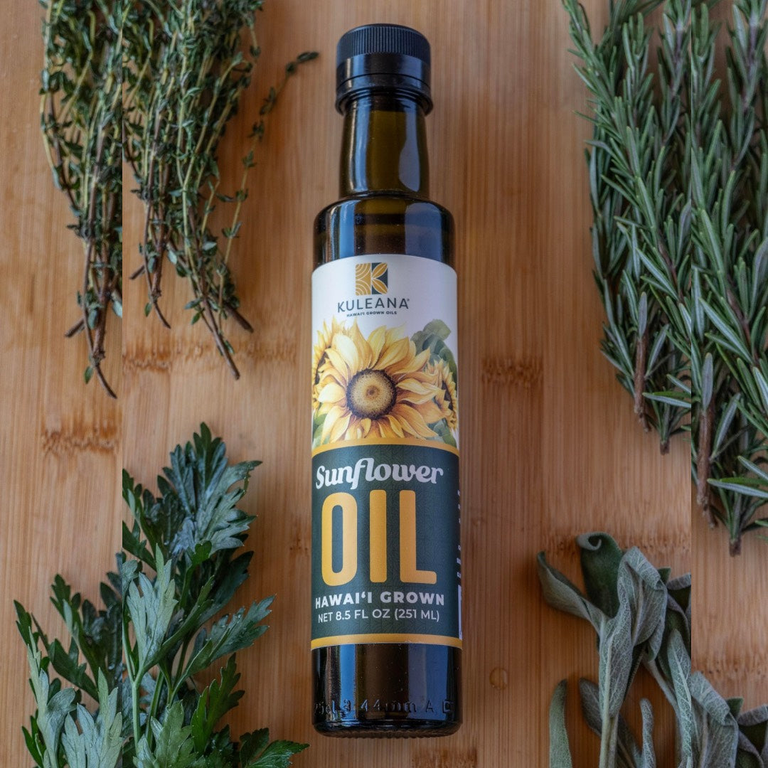 Bottle of Kuleana Sunflower Oil on a wooden surface with herbs around